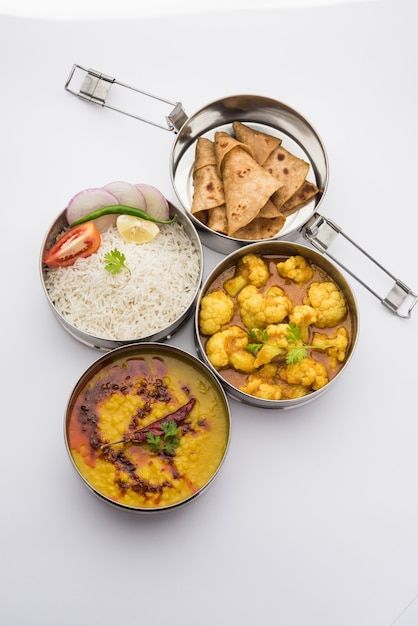indian vegetarian lunch box or tiffin made up of stainless steel for office or workplace, includes dal fry, gobi masala, rice with chapati and salad premium photo